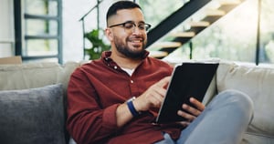 Reading, glasses and happy man relax with tablet on sofa for social media_846548069-min