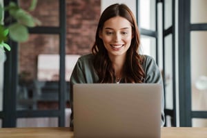 smiling woman working with laptop while sitting at table_396816953-min